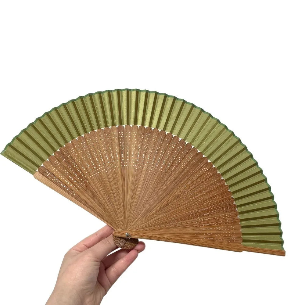 A hand holds an elegant bamboo folding fan with a classic design, showing the pleated fan blades.