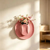 A pink ceramic wall vase holder with a floral arrangement is displayed on a light-colored wall.
