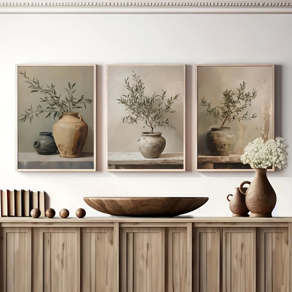 Three framed canvas prints featuring olive trees in terracotta pots displayed on a wooden shelf.