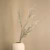 A sprig of artificial silk lover grass in a white ceramic vase against a neutral background.
