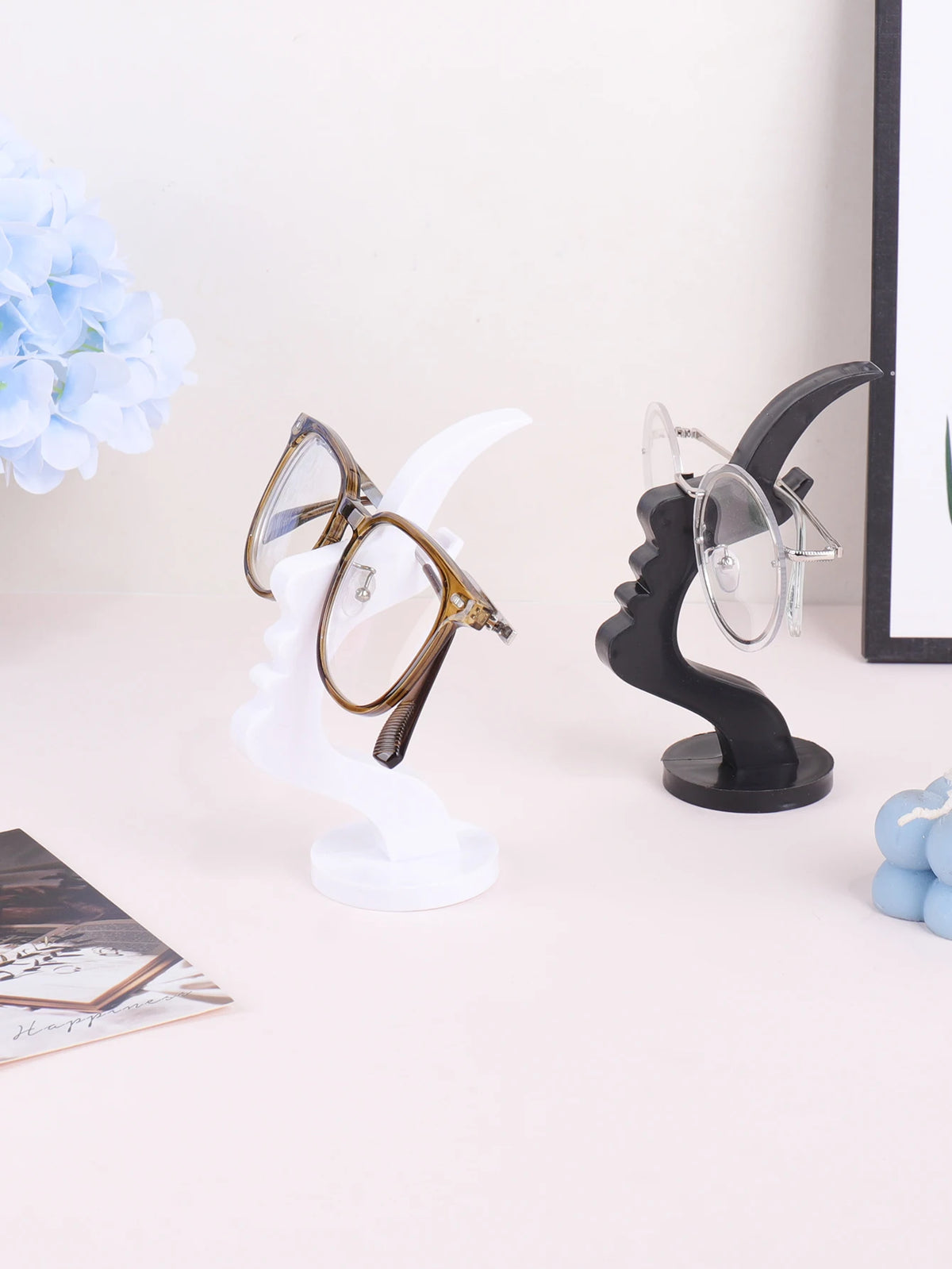A minimalist black glass holder displaying a pair of round tortoiseshell eyeglasses on a white display stand.