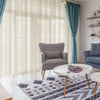 Light blue linen sheer curtains hanging in a living room with a gray armchair and white coffee table.