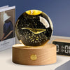 A dark glass crystal ball decoration with a gold-colored object inside, resting on a wooden base.