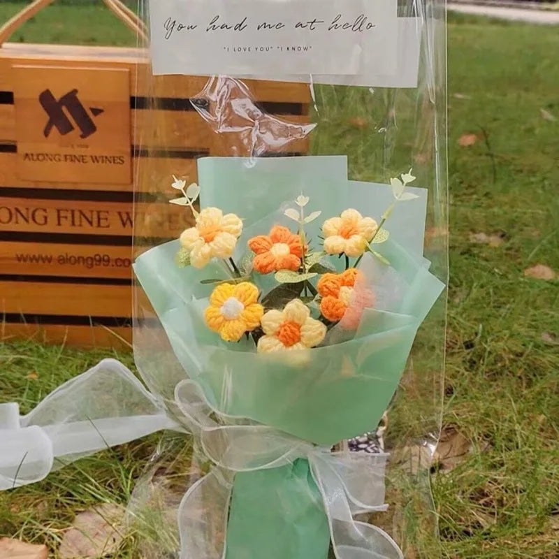 A handmade crochet flower bouquet featuring yellow and orange flowers wrapped in clear cellophane.