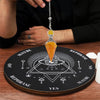 A hand holds a crystal pendulum suspended over a wooden board with various symbols for dowsing and divination.