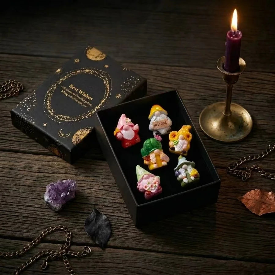 A set of Halloween witch mini dwarf resin figurines in various colors displayed on a dark wooden surface with a lit candle.