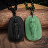 A pair of obsidian and jade pendant necklaces featuring religious figures, displayed on a wooden surface.