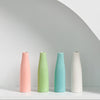Three ceramic mini vases in pink, lime green, and light blue standing on a white surface.