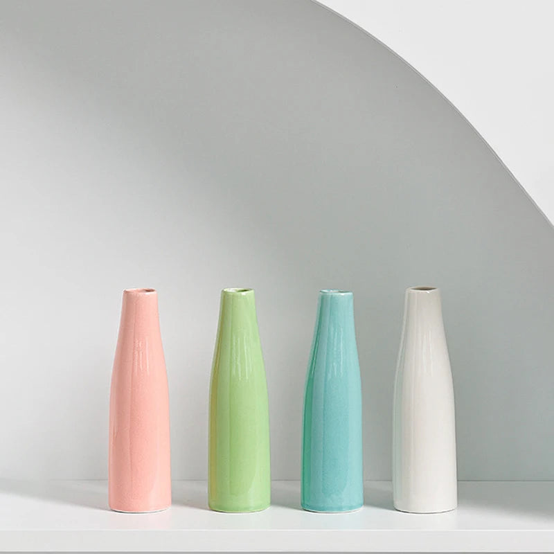 Three ceramic mini vases in pink, lime green, and light blue standing on a white surface.