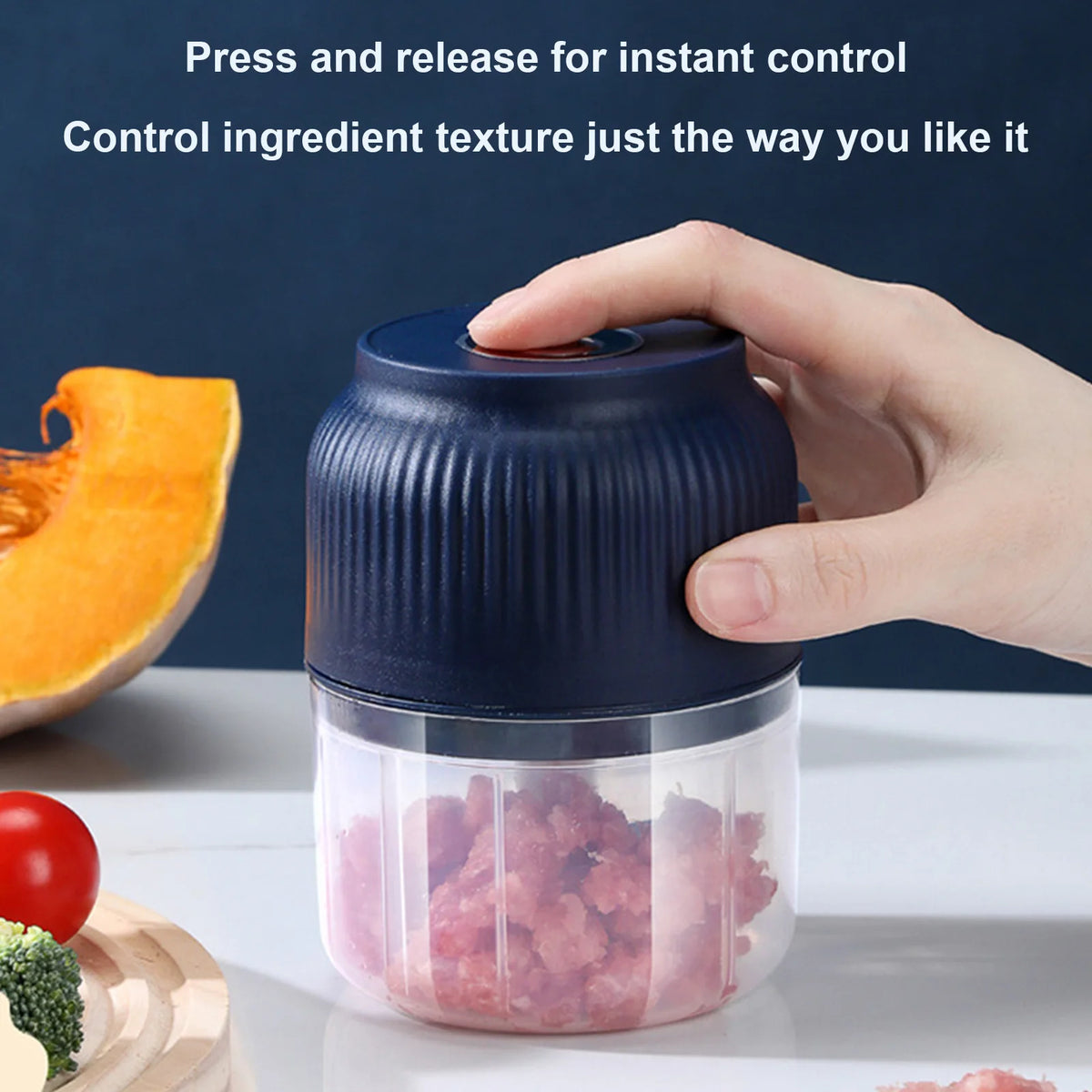 A hand is pressing a dark blue electric mini food chopper with a clear container filled with chopped ingredients.