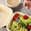 A fork is shown lifting a green salad with tomatoes from an open white plastic container.