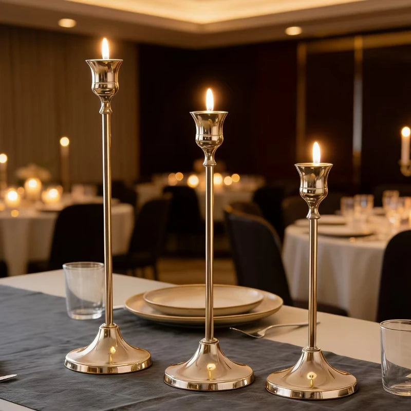 Three elegant metal candlesticks with lit candles displayed on a table setting.
