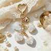 Gold heart-shaped rhinestone keychain and bag charm resting on white lace fabric with pearls