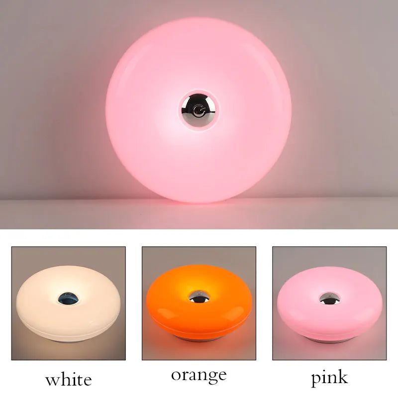 Drei Versionen einer donutförmigen, wiederaufladbaren Wandlampe in Weiß, Orange und Pink.