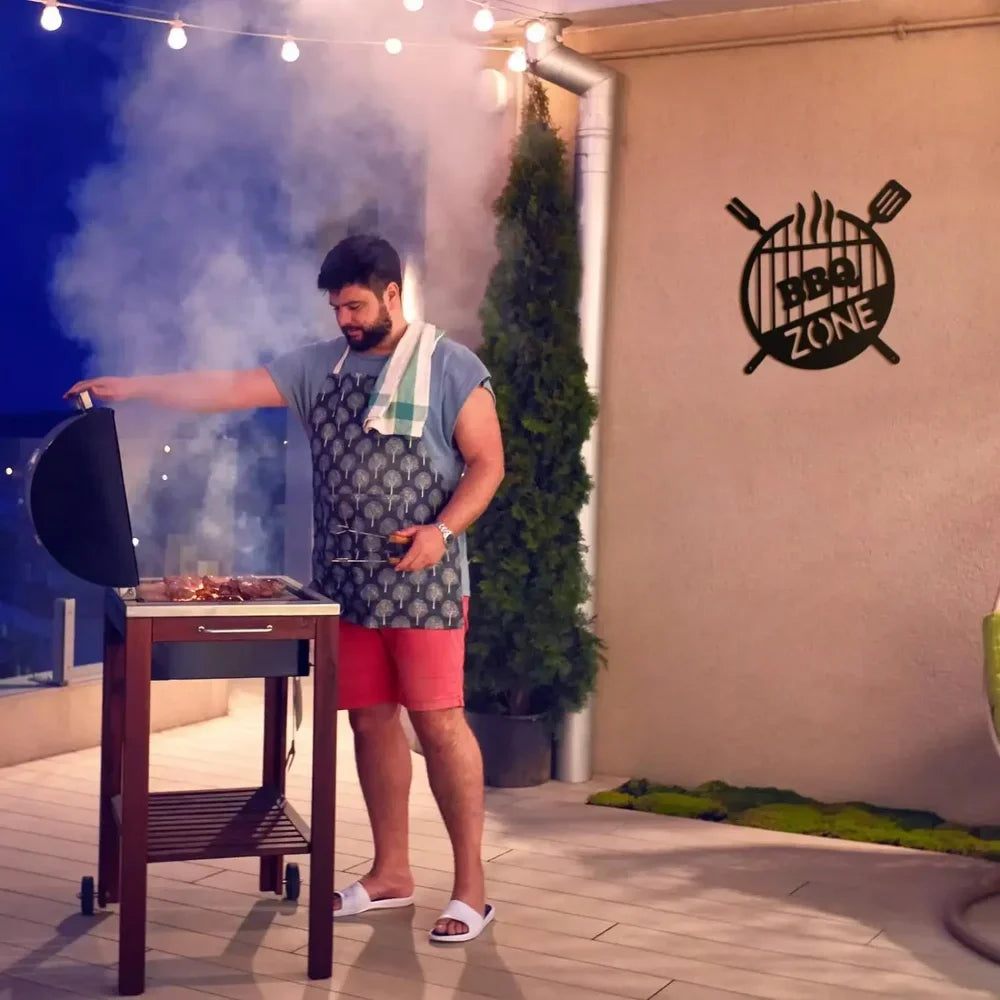 A man grilling food outdoors with smoke, in front of a wall sign that reads BBQ ZONE.