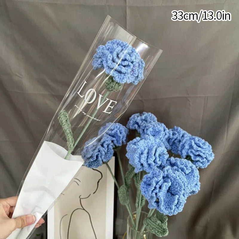 A bouquet of handmade blue crochet tulips displayed in a clear glass vase against a gray background.