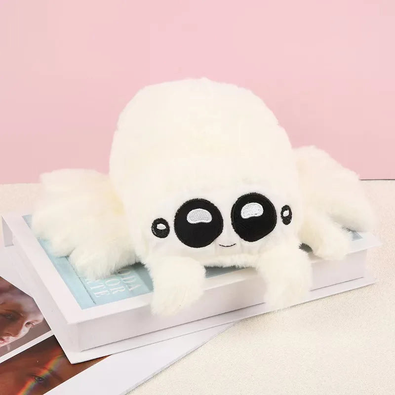 A white Lucas the Spider plush toy with large black eyes and soft limbs resting on a white box.