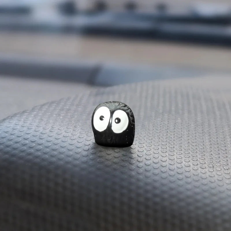 Un petit ornement noir en forme de tête d'elfe avec de grands yeux blancs, posé sur une surface texturée sombre.