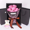 A gift box containing a bouquet of pink roses and a white plush bear, tied with a ribbon.