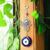 Silver hamsa hand amulet with a blue evil eye charm hanging on a wooden panel.