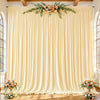 A floor-to-ceiling cream fabric backdrop with vertical pleats and floral greenery for an event setting.