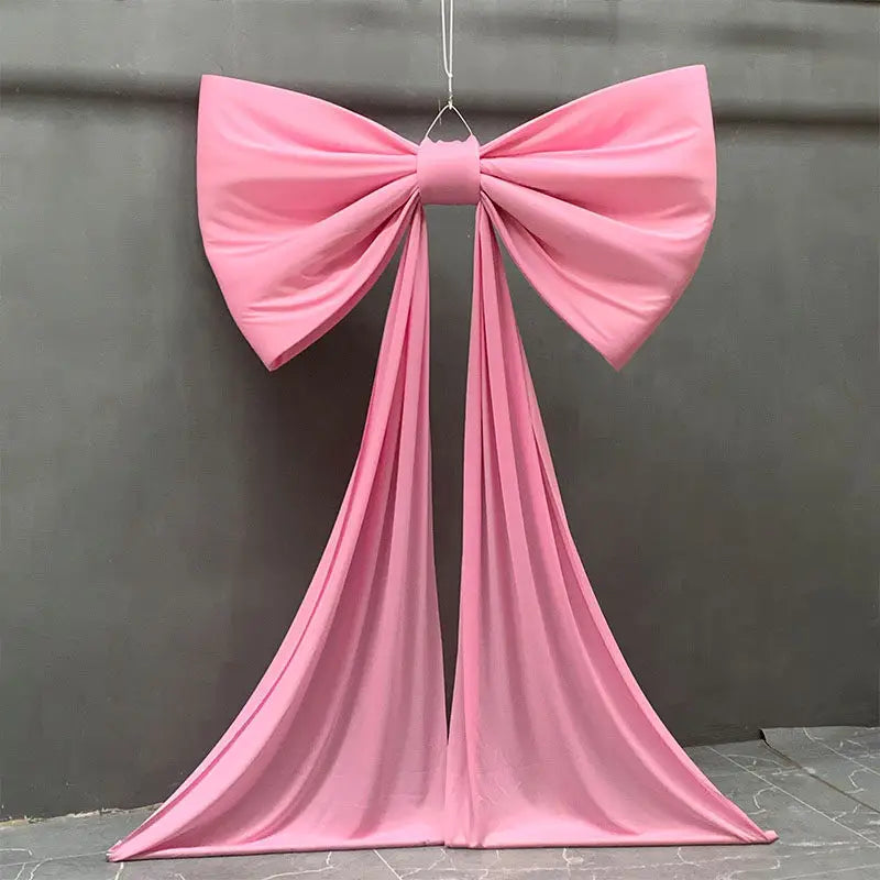 A pink satin bow with long tulle drapes hanging against a gray wall.