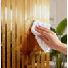 A hand wipes a metallic gold striped peel-and-stick wallpaper surface.