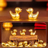 A set of small golden duck resin statues displayed on a wooden surface with additional ducks scattered nearby.