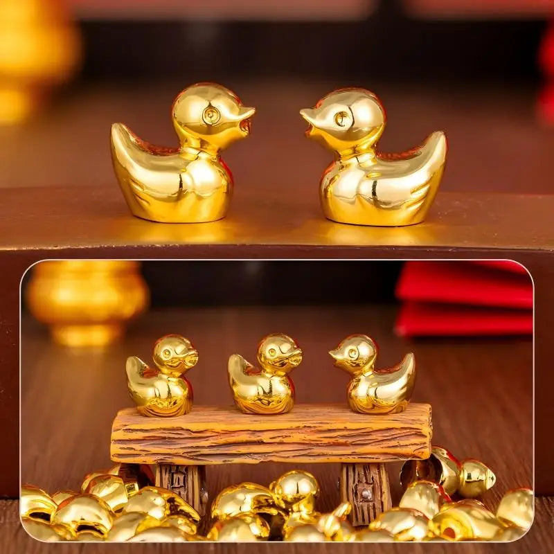 A set of small golden duck resin statues displayed on a wooden surface with additional ducks scattered nearby.