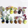 A collection of mini ceramic vases with artificial flowers in various colors and textures.