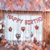 A display of pink and silver foil letter balloons spelling out Happy Birthday against a sheer curtain backdrop.