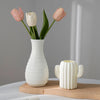 Eine weiße Keramikvase mit drei rosa und weißen Tulpen vor grauem Hintergrund.