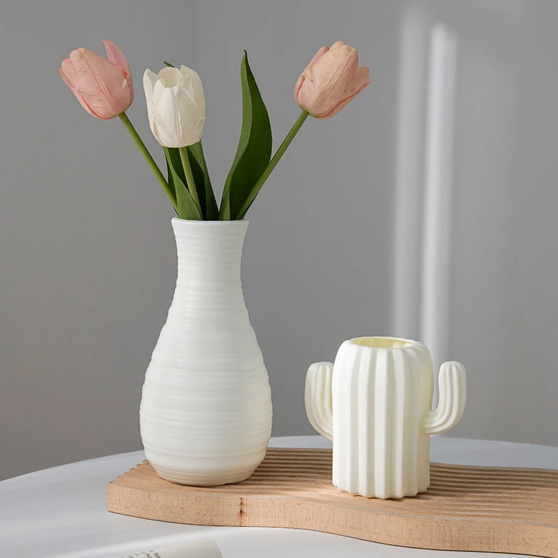 Eine weiße Keramikvase mit drei rosa und weißen Tulpen vor grauem Hintergrund.