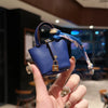 A hand holds a small navy blue leather handbag with a patterned wrist strap against a blurred indoor background.