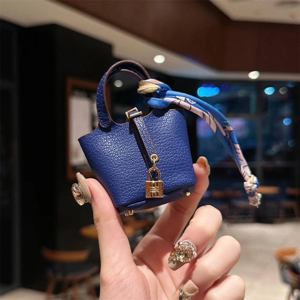 A hand holds a small navy blue leather handbag with a patterned wrist strap against a blurred indoor background.