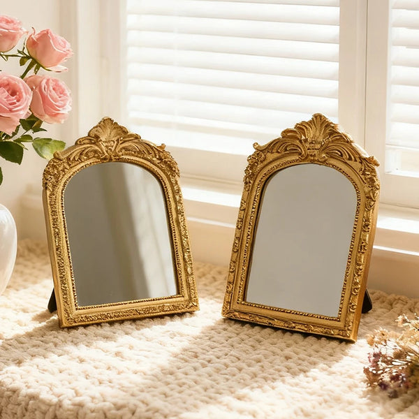 A vintage arched carved gold vanity mirror resting on a beige knitted surface near a window.