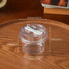 A clear plastic reusable pudding cup with a lid is shown on a wooden surface, with various dimensions marked.