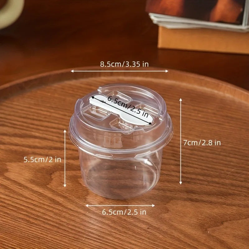 A clear plastic reusable pudding cup with a lid is shown on a wooden surface, with various dimensions marked.