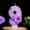 A purple glitter number candle shaped like the number 8 decorated with small flowers on a wooden surface.