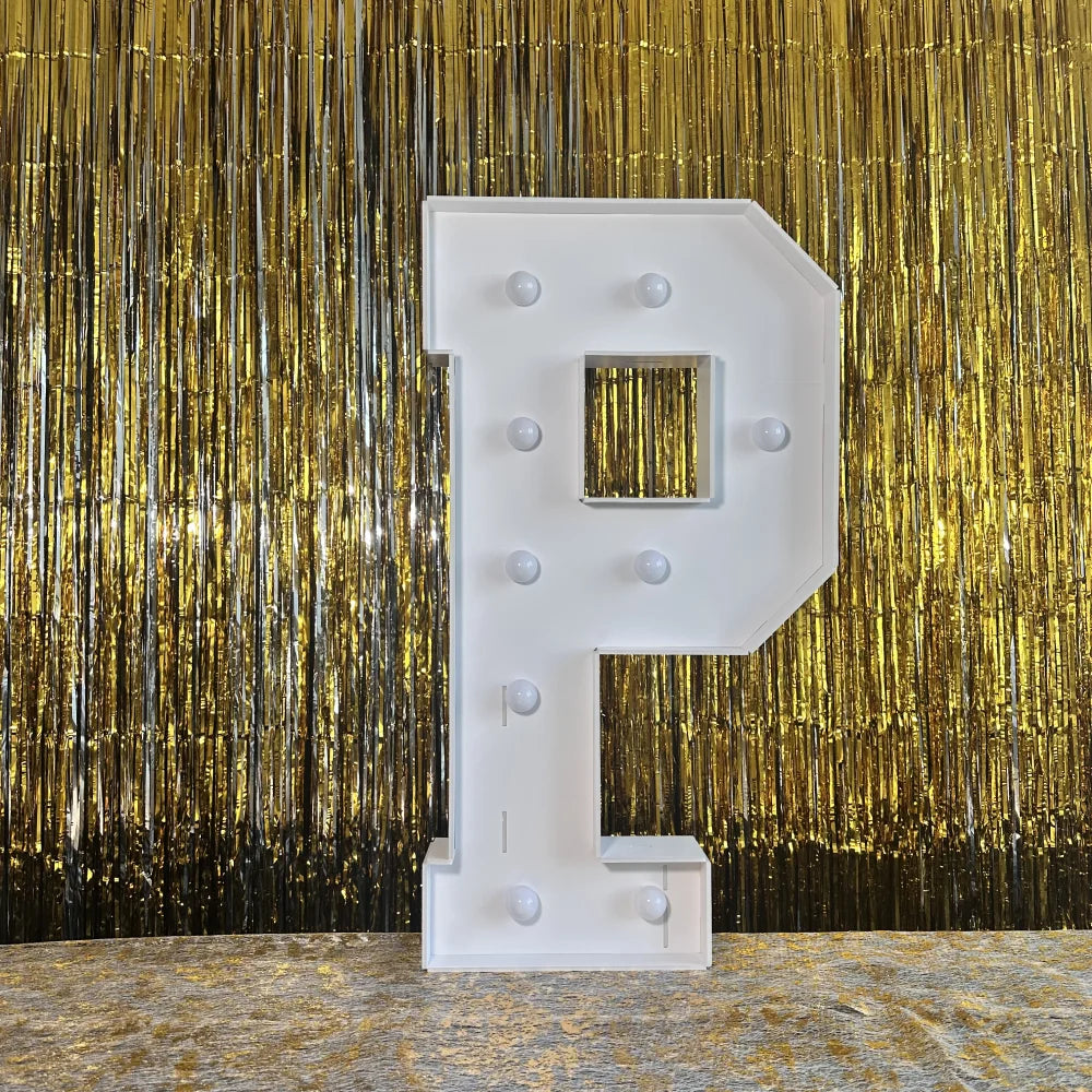 A large white marquee letter P with a mirrored insert displayed against a shimmering gold curtain backdrop.