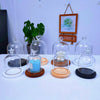 A collection of glass aromatherapy candle holders with wooden bases and dust-proof covers displayed on a white table.