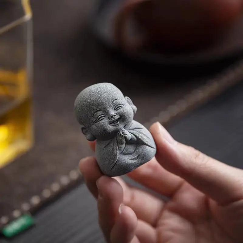 A hand holds a small, gray stone monk statue for meditation and Zen decor.