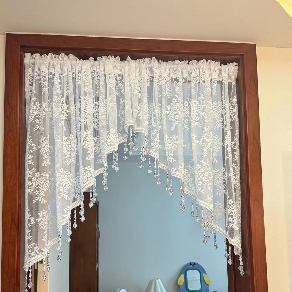 A sheer white beaded lace valance curtain with delicate floral patterns hanging in a wooden frame.