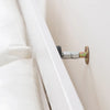 A close-up view of a silver adjustable bed stabilizer mechanism attached to a white wooden frame.