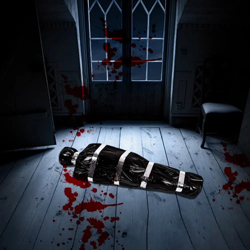 A realistic prop of a deceased victim wrapped in black plastic lies on a wooden floor stained with red blood.