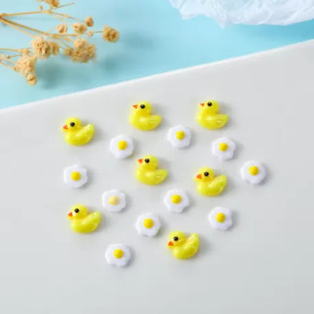 Una colección de 50 adornos de uñas de tortuga amarilla mini y coloridos esparcidos sobre una superficie blanca.