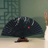 A dark blue hand folding fan with white floral designs displayed on a white surface.