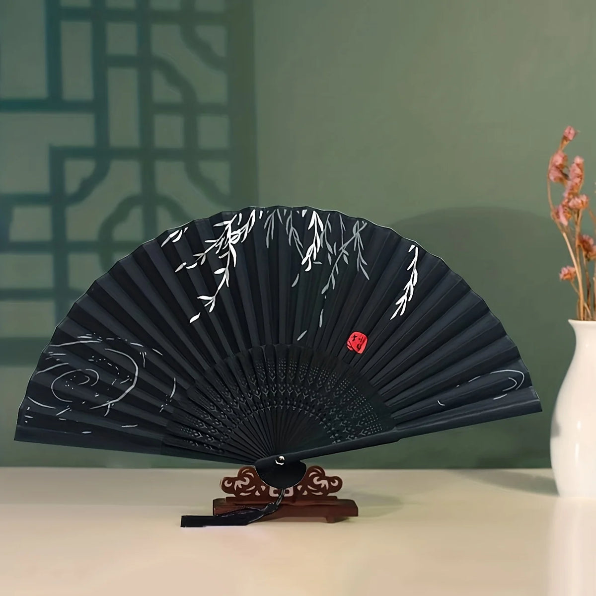 A dark blue hand folding fan with white floral designs displayed on a white surface.