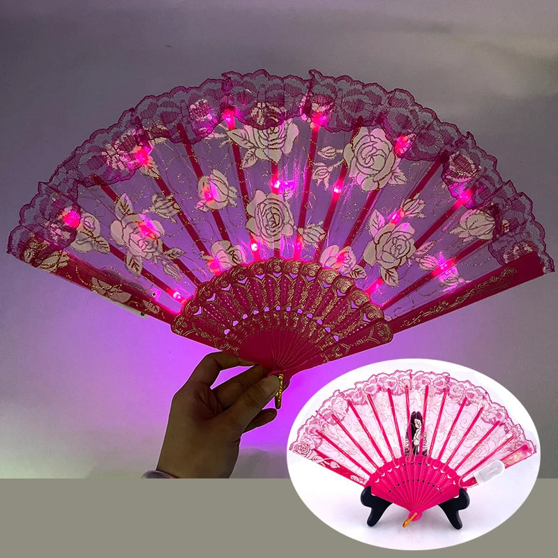 A pink LED dancing hand fan with rose patterns is held against a purple background.