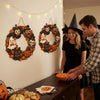 A woman is hanging a vintage Halloween wooden wreath on a white wall.